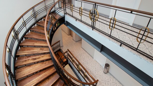 Una escalera de caracol con escalones de madera y barandillas de metal, que conduce a un piso superior con suelo estampado.
