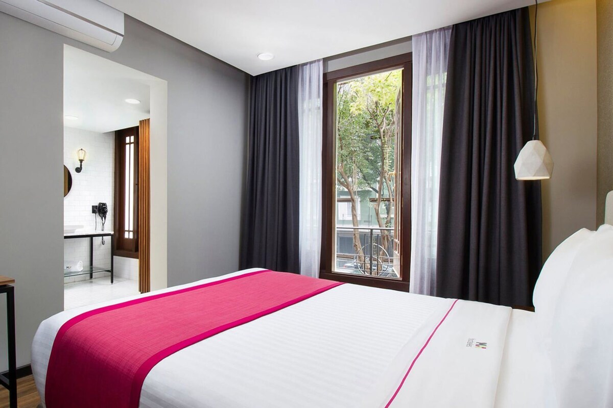 A hotel room with a bed, a desk, a chair, a TV, and a window with curtains.