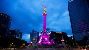 Panorama nocturno de una ciudad con un monumento iluminado destacado, que presenta estatuas y una figura en su cima.