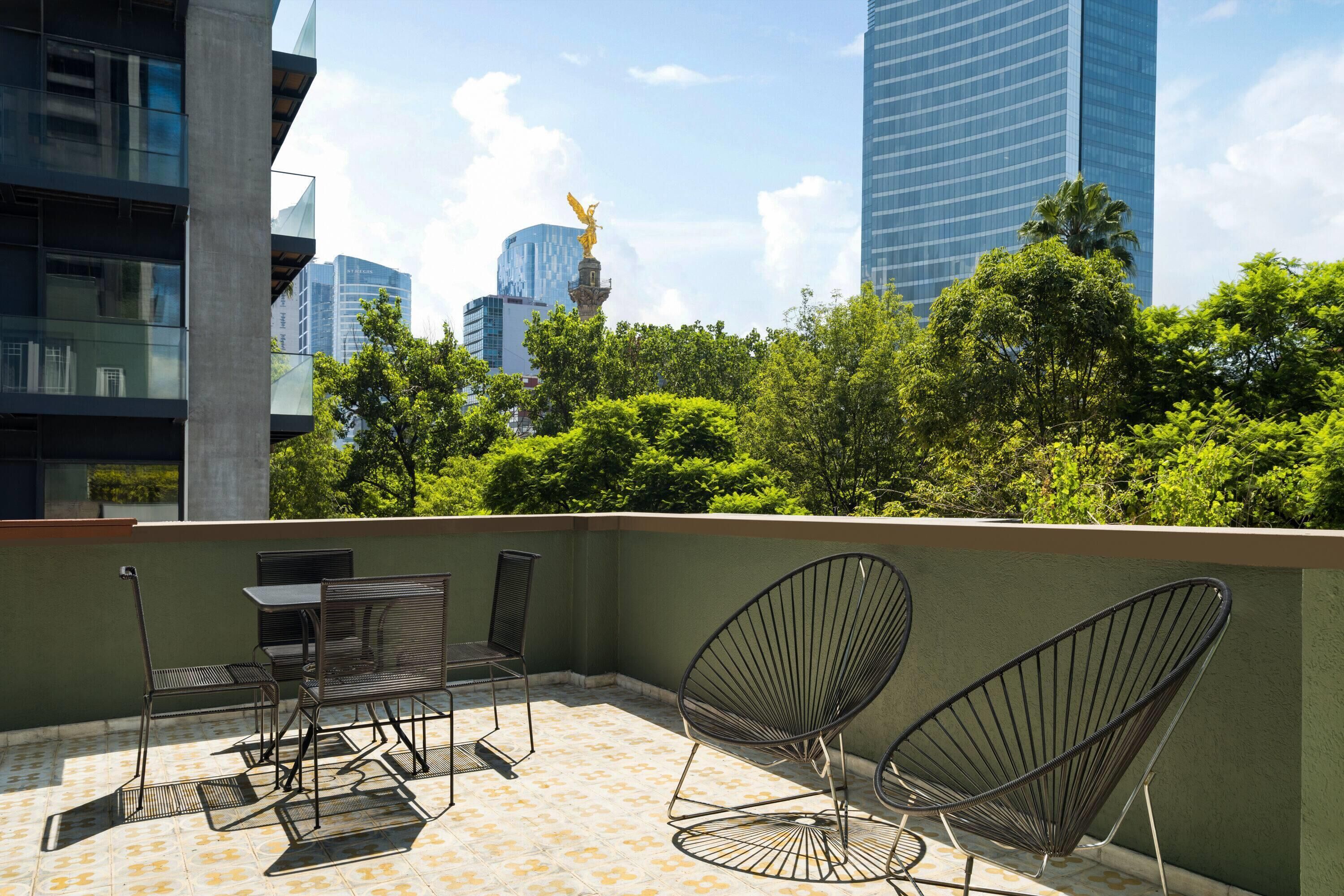 A rooftop terrace with outdoor furniture, a statue, and a view of city buildings.