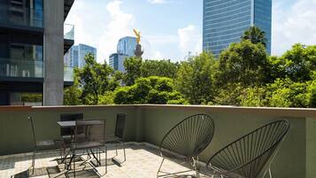 A rooftop terrace with outdoor furniture, a statue, and a view of city buildings.