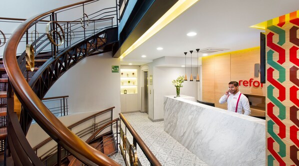 Zona de recepción de un hotel con mostrador de mármol, escalera de caracol y diseño moderno.
