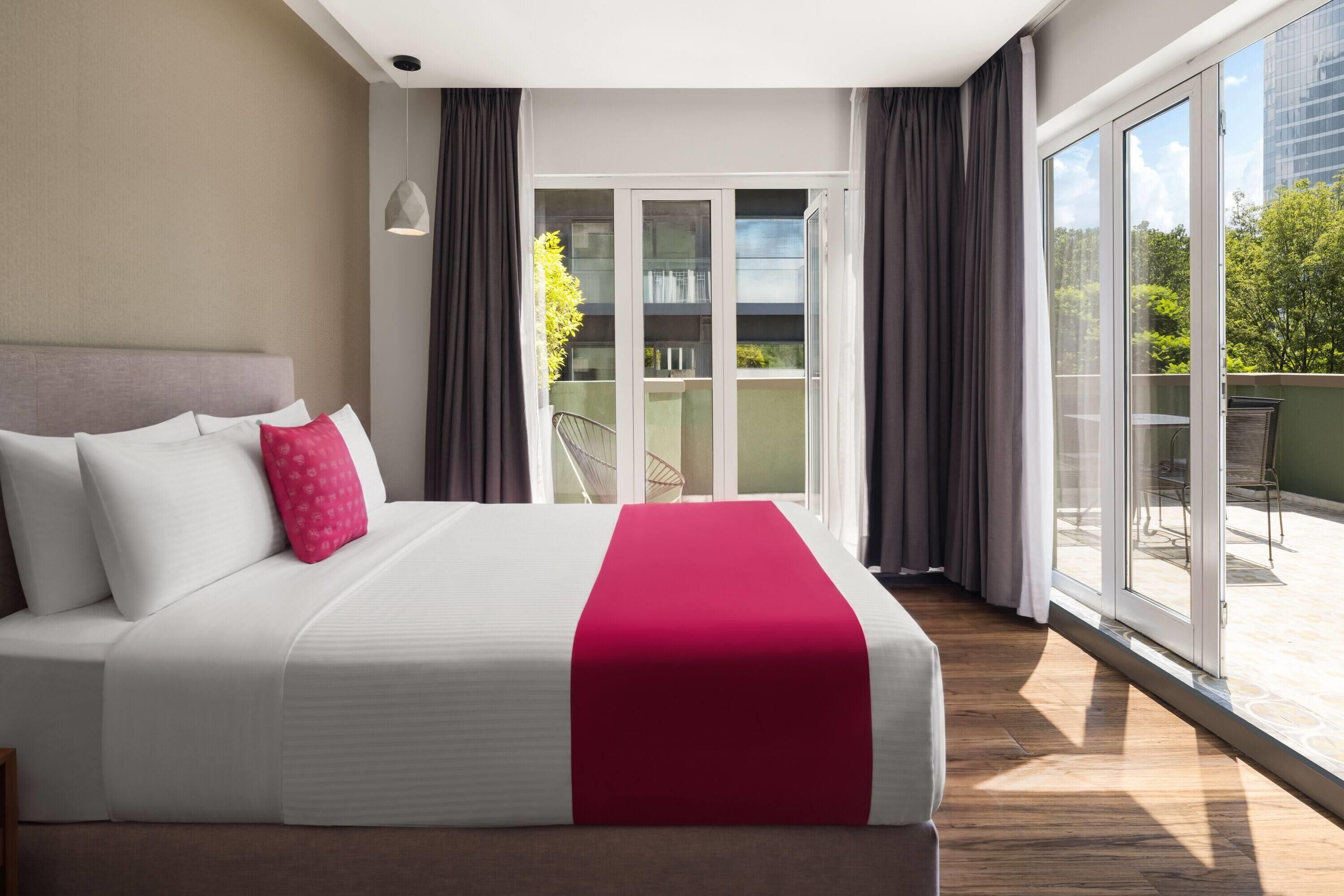 Una habitación de hotel con una cama grande, un balcón con vistas y un ventanal corredero.