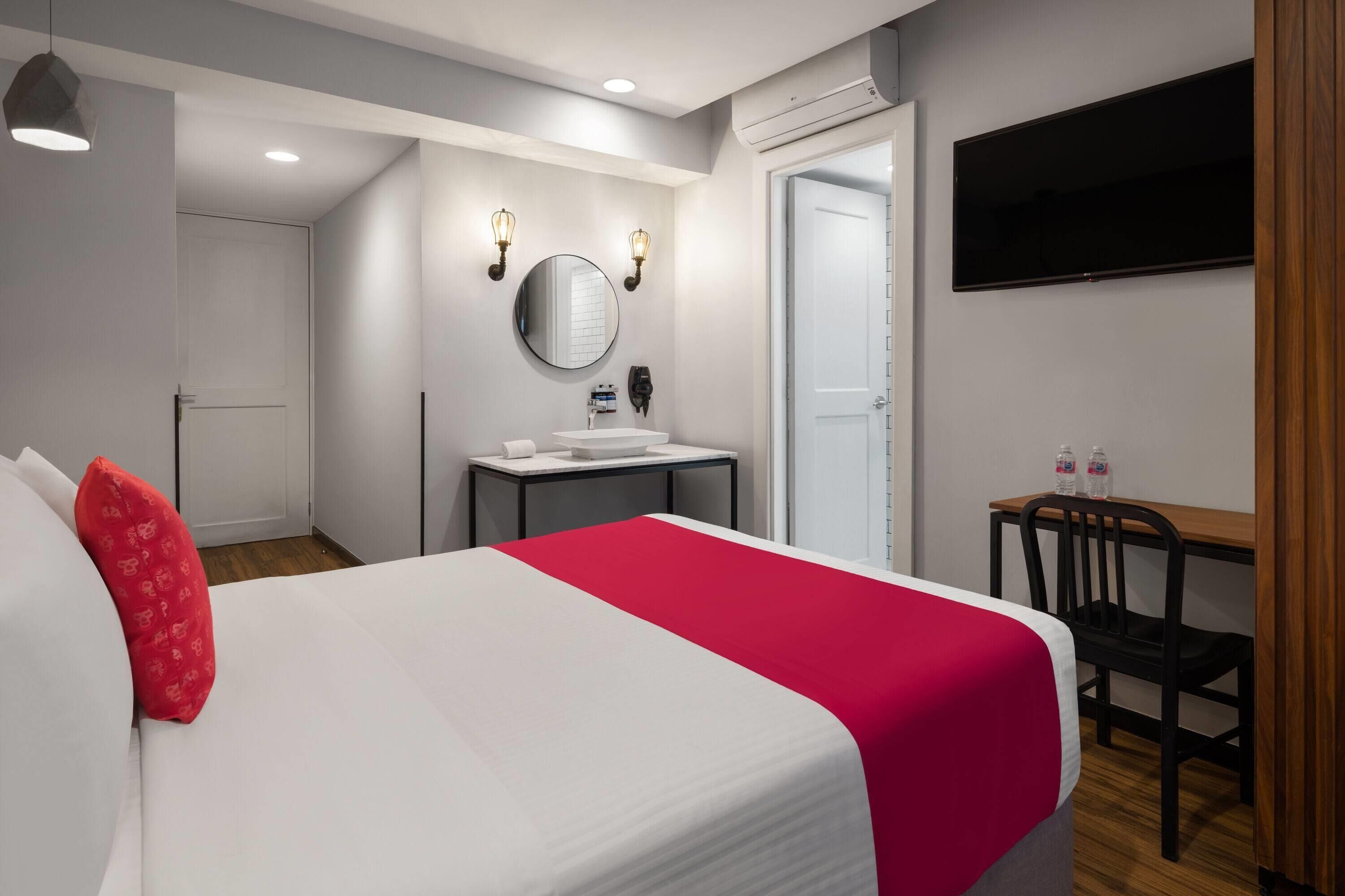 Una camera d'albergo con un letto, una scrivania, uno specchio, una televisione e un bagno.