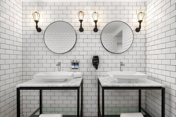 Un baño moderno con dos lavamanos, espejos redondos e iluminación empotrada.
