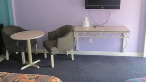 Una habitación con una mesa redonda, dos sillones, un televisor montado en la pared y una pequeña mesa blanca con un rascador para gatos.