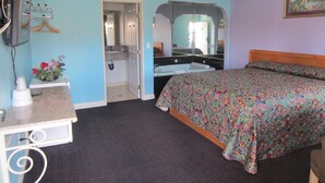 Un dormitorio con cama, escritorio con espejo, televisor y baño visible a través de una puerta abierta.