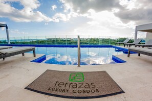 Un espace piscine sur le toit, doté de chaises longues, offrant une vue dégagée sur le paysage urbain, et un panneau indiquant « terrazas, appartements de luxe ».