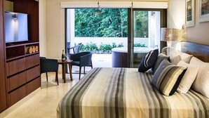 Een slaapkamer met een groot bed, een televisie, een klein tafeltje met stoelen en uitzicht op groen via de schuifdeuren.