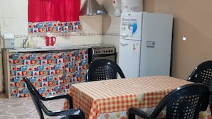 A compact kitchen with a refrigerator, stove, and a table with chairs. - La Casa (San Lorenzo)