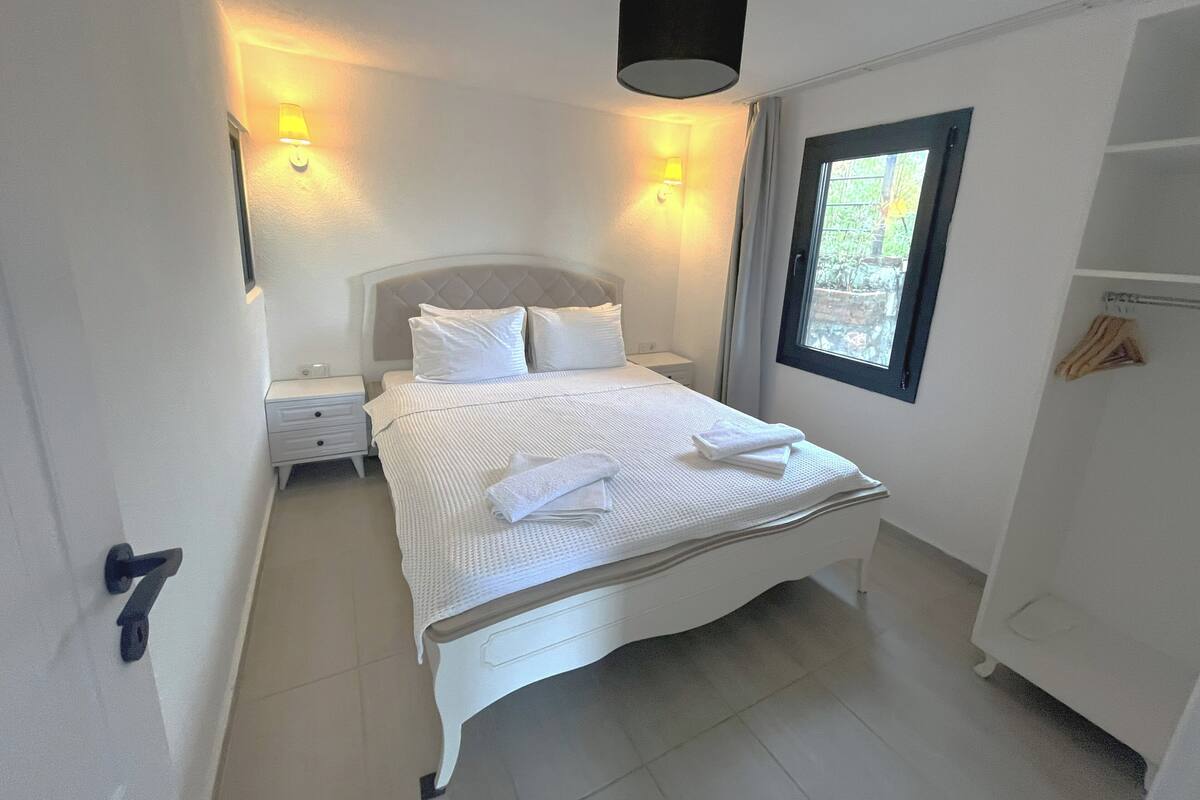 A neatly arranged bedroom with a bed, bedside lamps, a window, and a wardrobe.