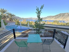 A balcony with a pool, two chairs, a table, and a view of a mountainous landscape and the sea. - Gala Selimiye (Marmaris)
