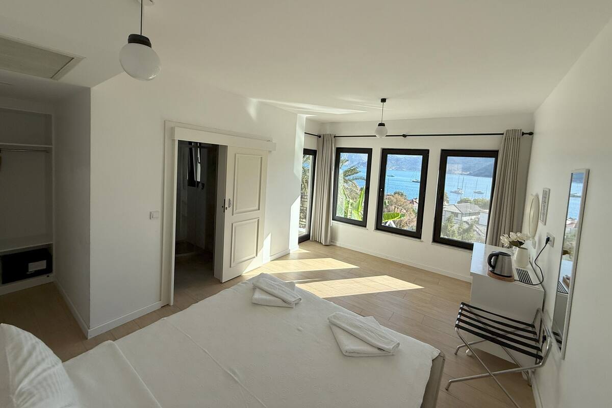 A spacious bedroom with a large bed, a walk-in closet, and multiple windows offering a view of the sea.