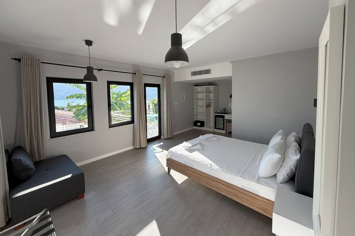A modern bedroom with a large bed, a desk, and a view of the outdoors.