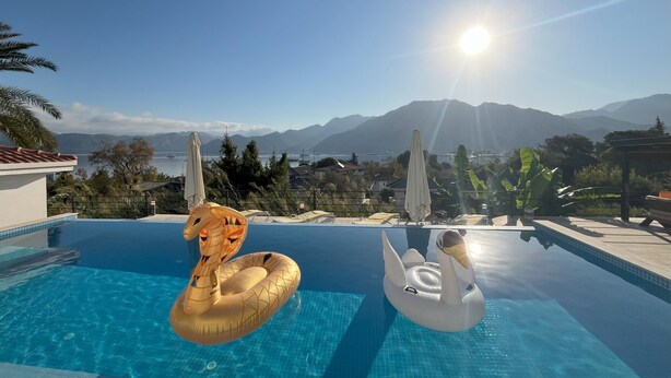 A swimming pool with two inflatable swan floats, a clear view of mountains, and a sunny sky. - Gala Selimiye (Marmaris)