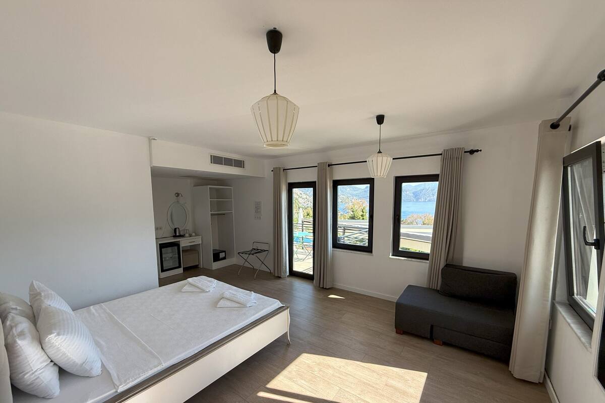 A modern hotel room with a large bed, a seating area, a desk with a mirror, and a view of the outdoors.