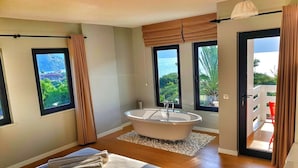 A modern bedroom with a large bed, a freestanding bathtub, and a balcony with a view of the ocean. - Gala Selimiye (Marmaris)
