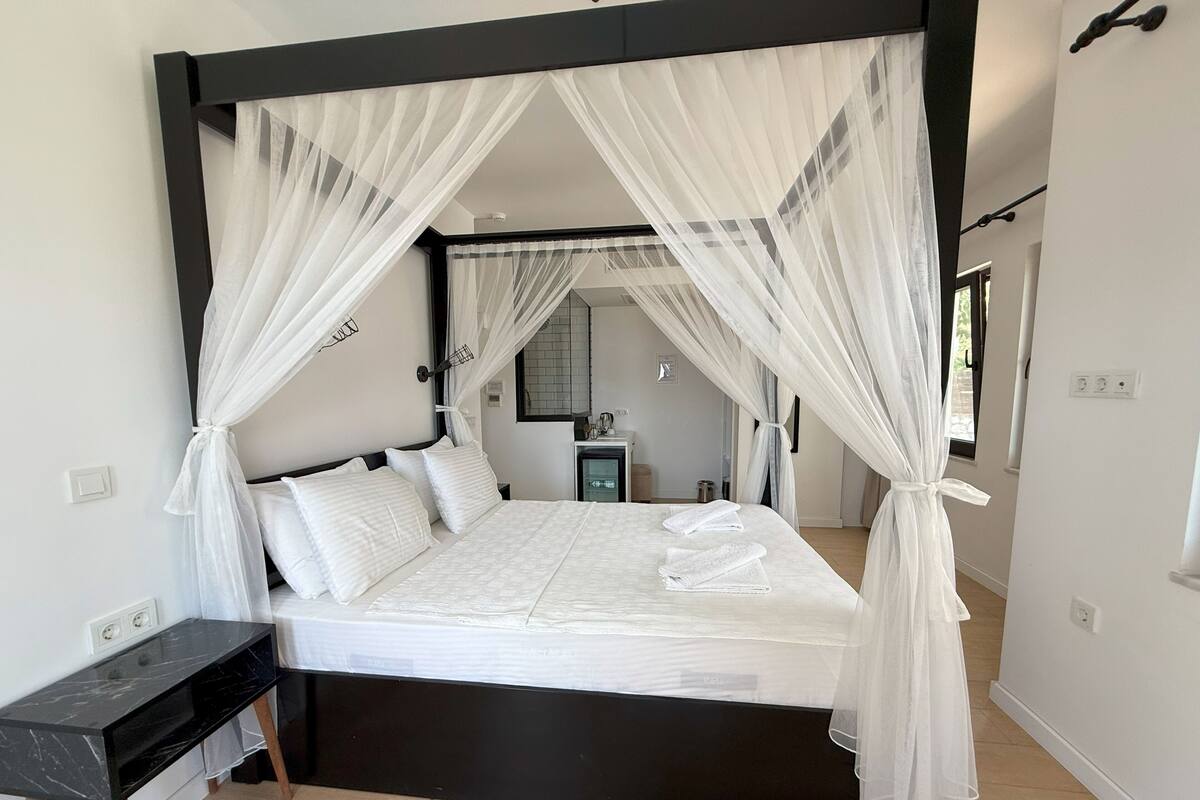 A modern bedroom with a four-poster bed, white bedding, and sheer canopy curtains.