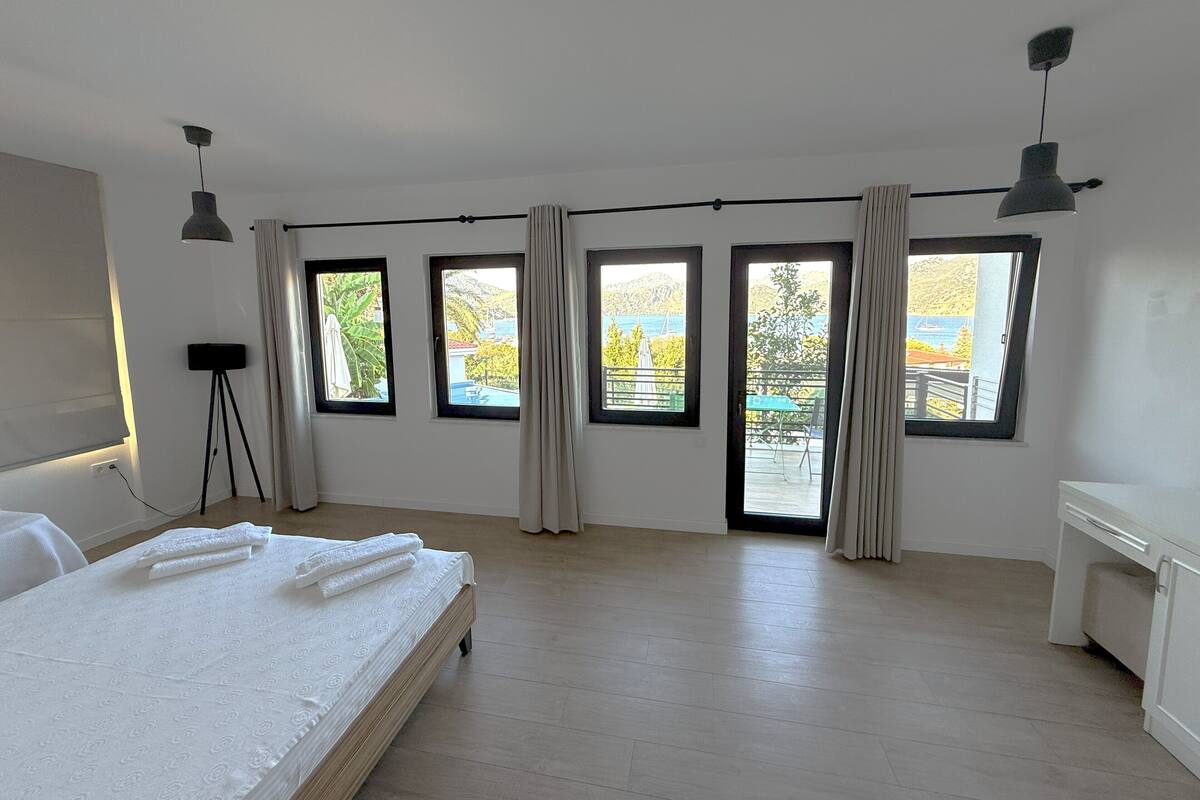 A modern bedroom with a large bed, multiple windows, and a view of the outdoors.