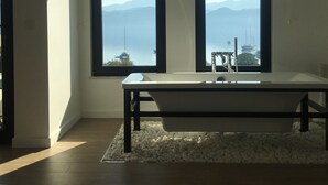 A modern bathroom with a bathtub, large windows, and a view of mountains and water. - Gala Selimiye (Marmaris)