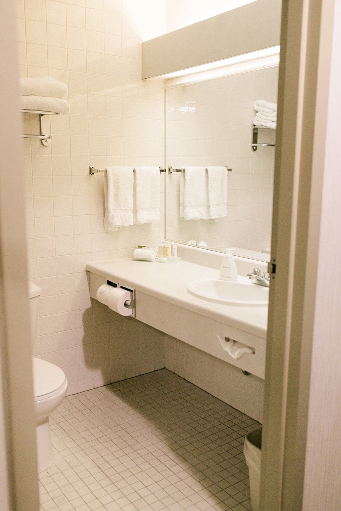 Un baño con inodoro, lavabo, espejo y dos toallas colgadas en la pared.