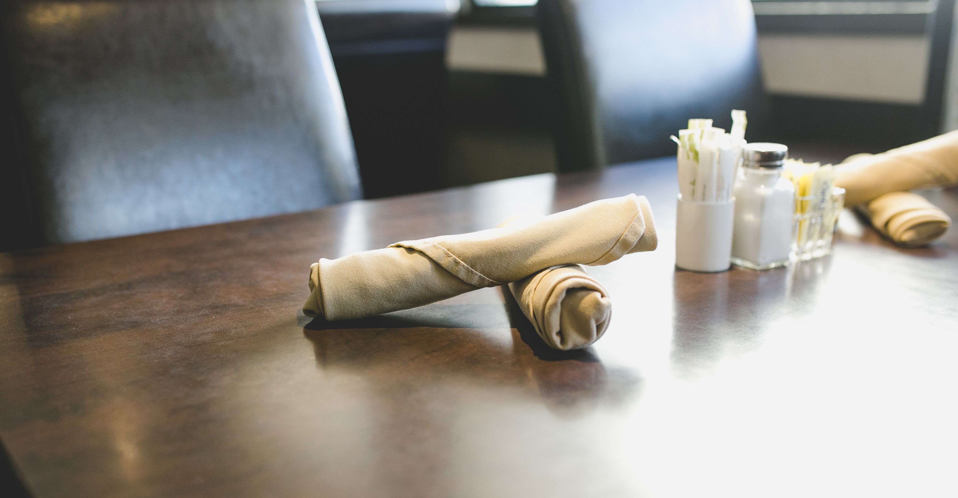 Une table bien dressée, avec une serviette pliée, un verre d’eau et un petit récipient contenant des couverts.
