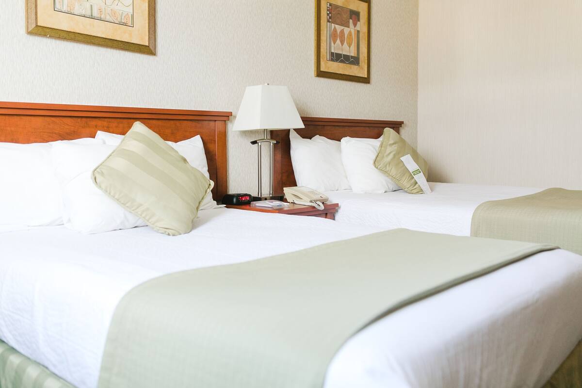 A hotel room with two beds, a bedside table with a lamp, a phone, and a tray with a book.