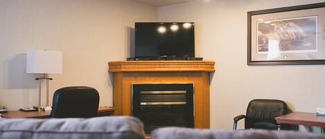 Habitación de hotel con chimenea, un televisor montado encima, un cuadro en la pared, un escritorio con lámpara y un sofá.