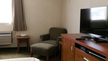 Quarto de hotel com uma cama, televisão, escrivaninha de madeira, cadeira e uma pequena mesa com controle remoto.