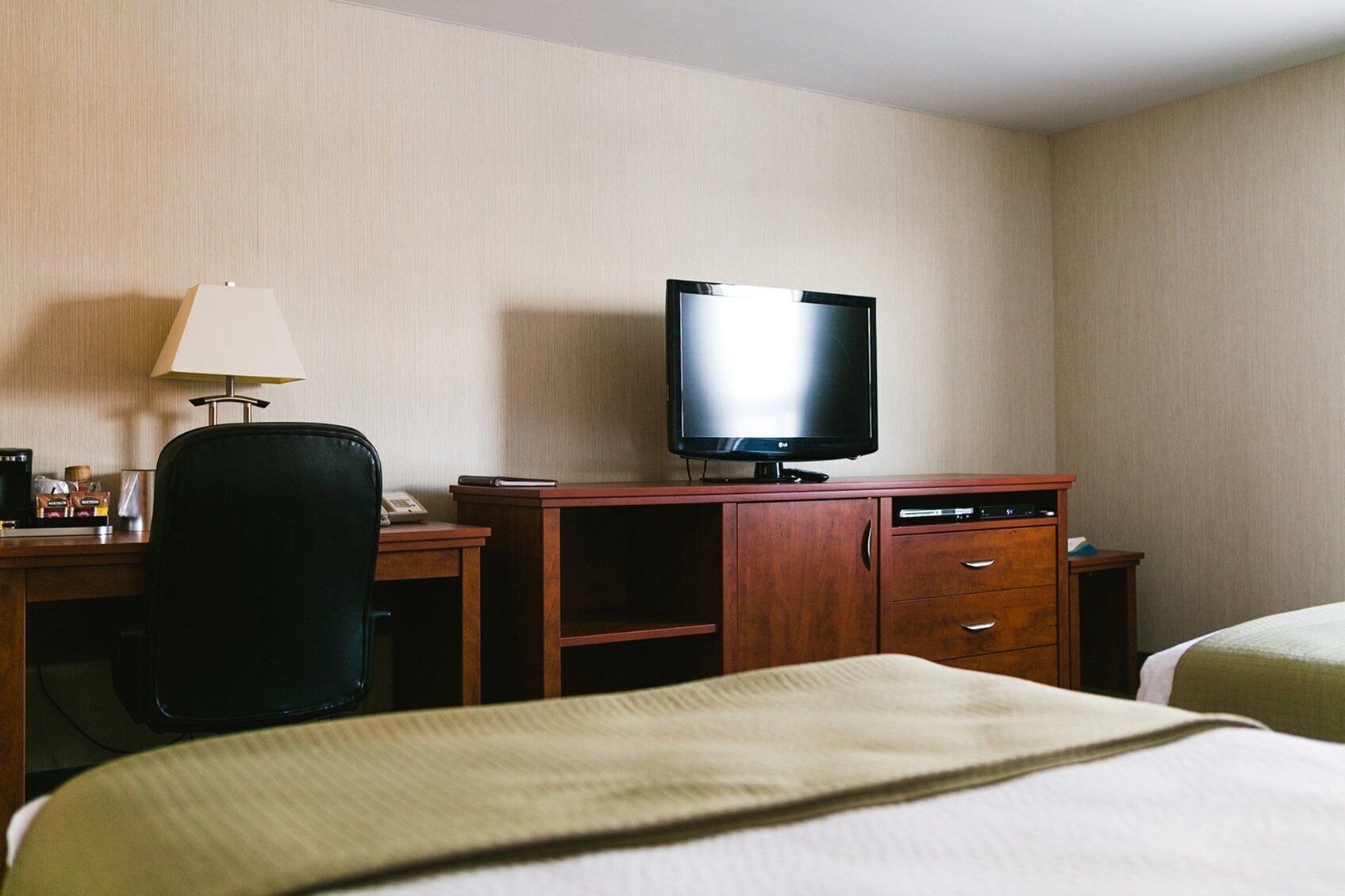 Ein Hotelzimmer mit einem Bett, einem Schreibtisch mit Fernseher, einer Lampe und einer Kaffeemaschine.