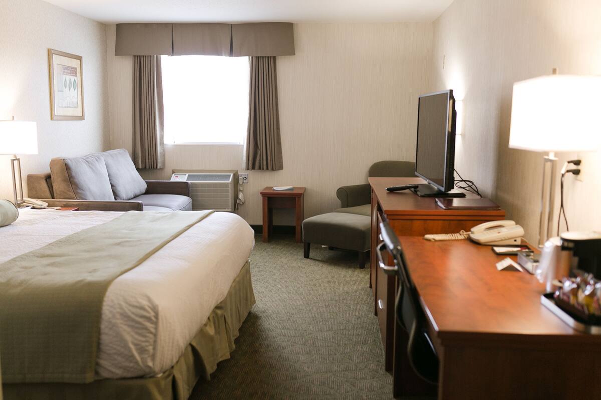 A hotel room with a bed, a desk, a television, a telephone, and a window with curtains.