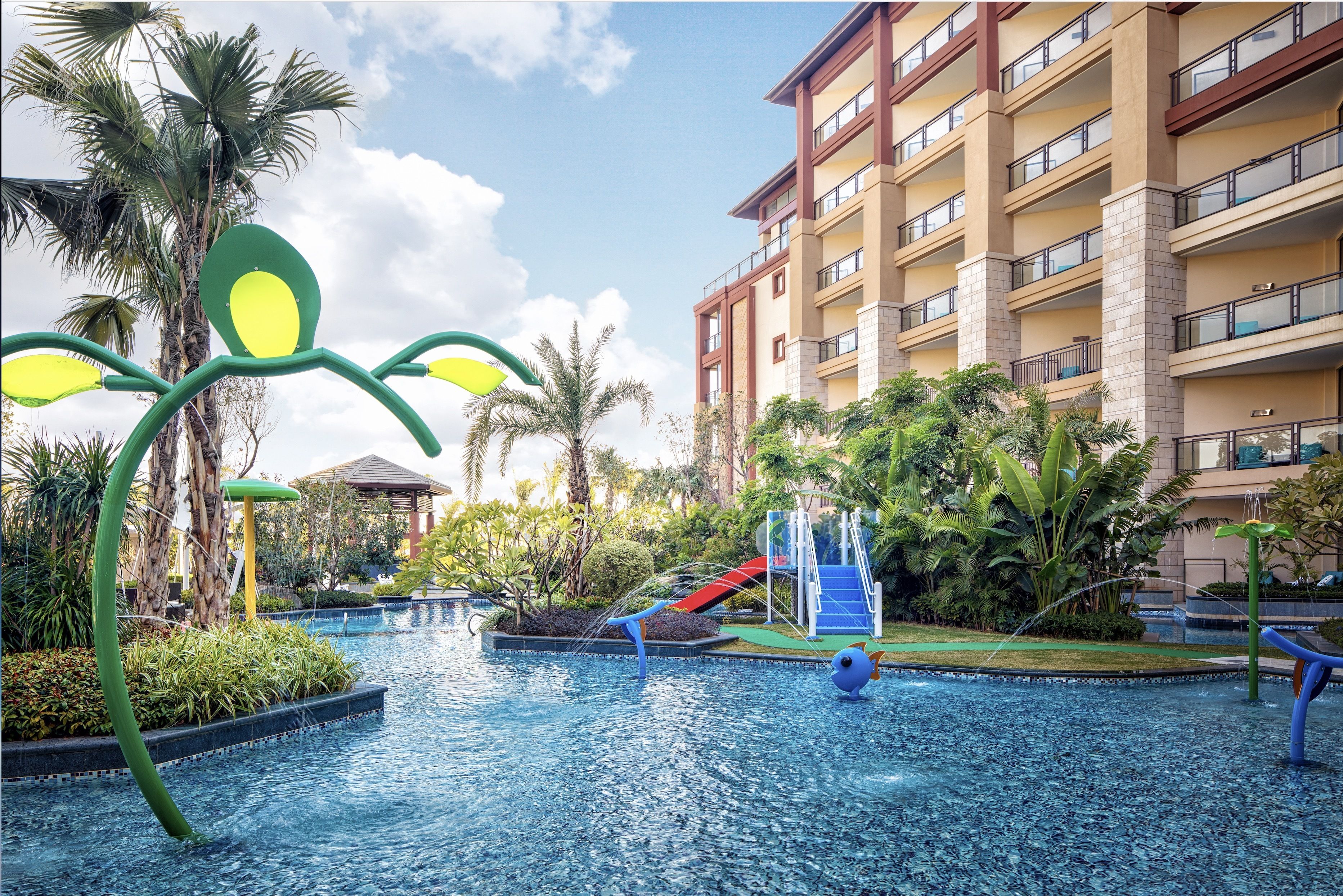 A hotel pool area with a slide, palm trees, and a building with balconies.