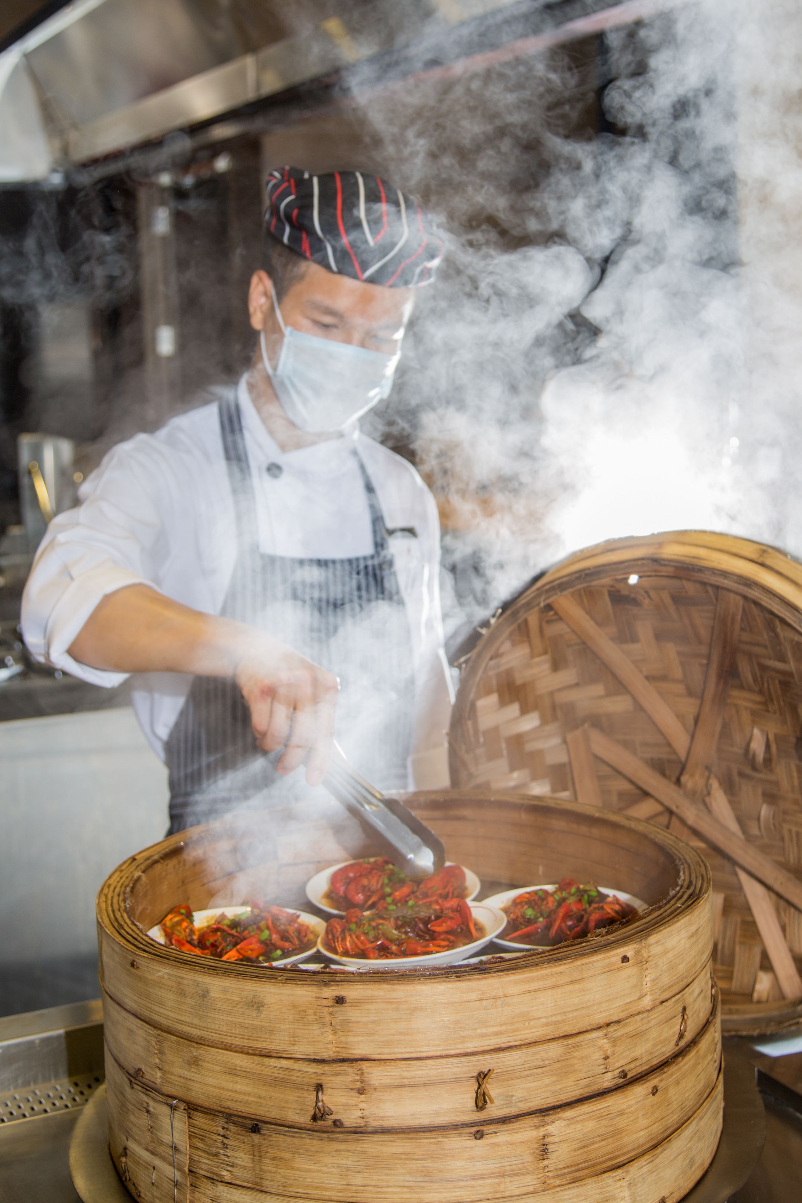 Un chef preparando comida en una cocina con un conducto de vapor y una vaporera de bambú tradicional.