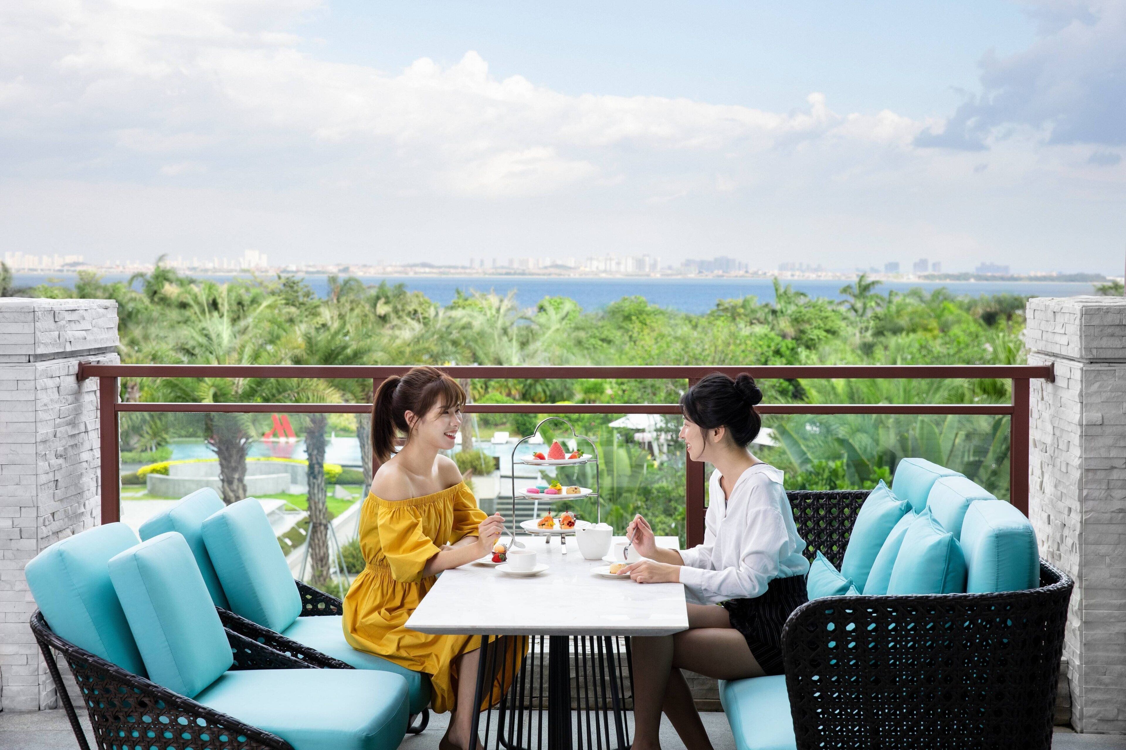 A terrace with wicker chairs, a table, and a view of a cityscape and greenery.