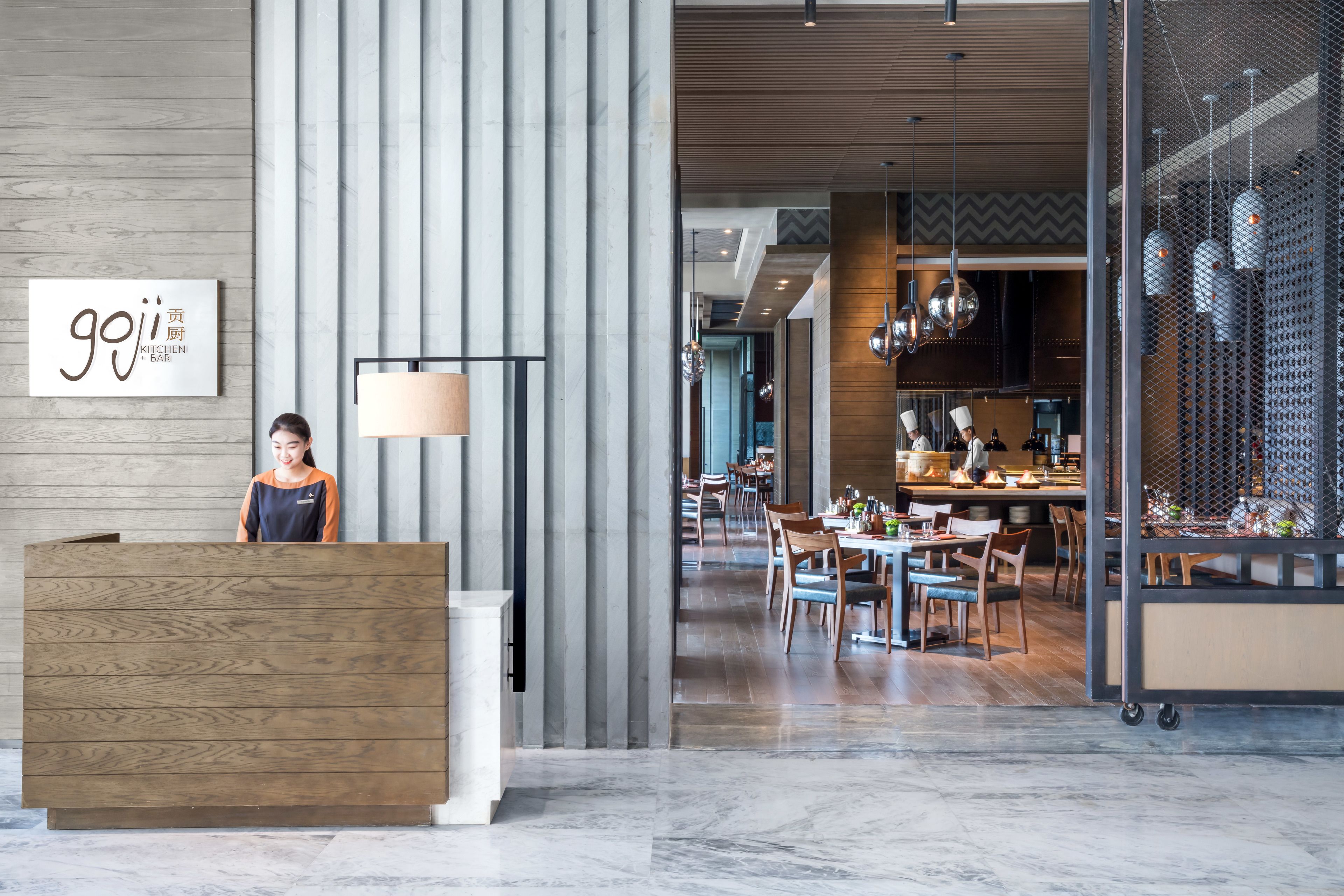 Un moderno vestíbulo de hotel con mostrador de recepción, pared de madera y comedor con mesas y sillas.