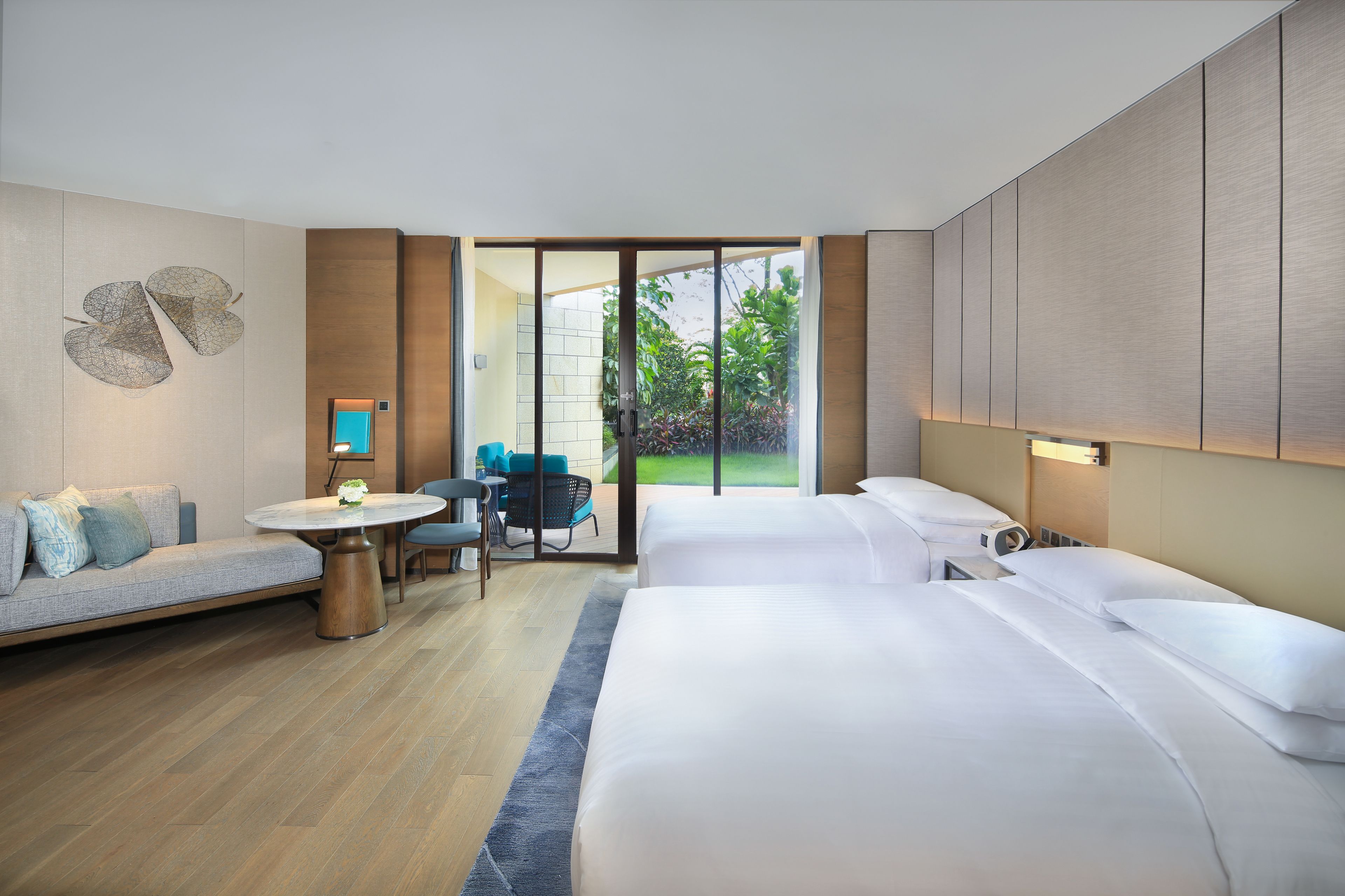 Una habitación de hotel moderna con una cama grande, un sofá, una mesita y vistas al jardín a través de una puerta corrediza.
