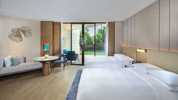 Una habitación de hotel moderna con una cama grande, un sofá, una mesita y vistas al jardín a través de una puerta corrediza.