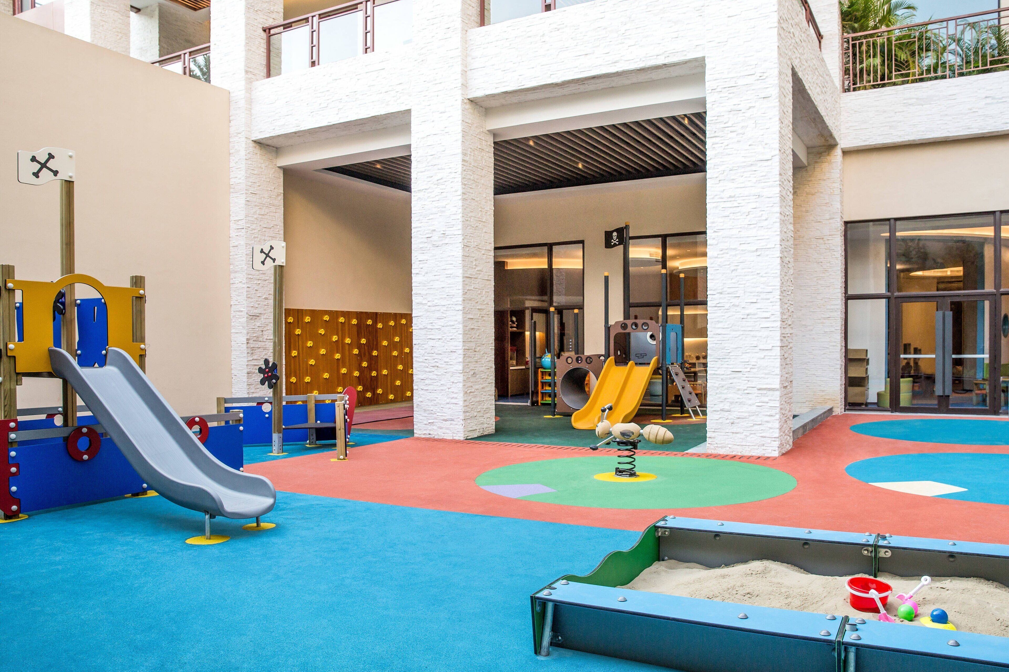 A children's play area with slides and climbing structures, surrounded by a multi-level building with large windows.