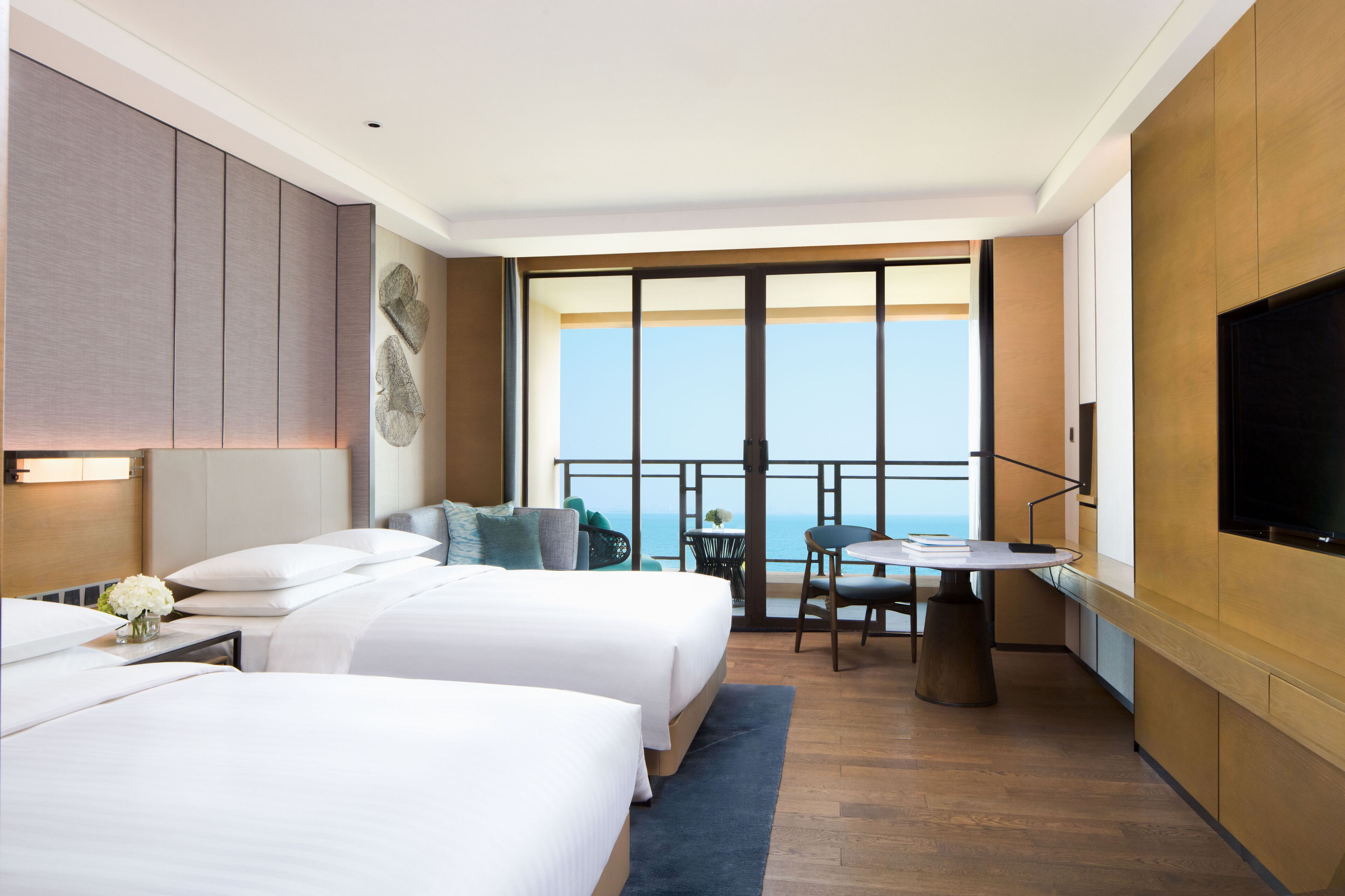 A hotel room with two beds, a balcony with a view, a TV, and a small table.