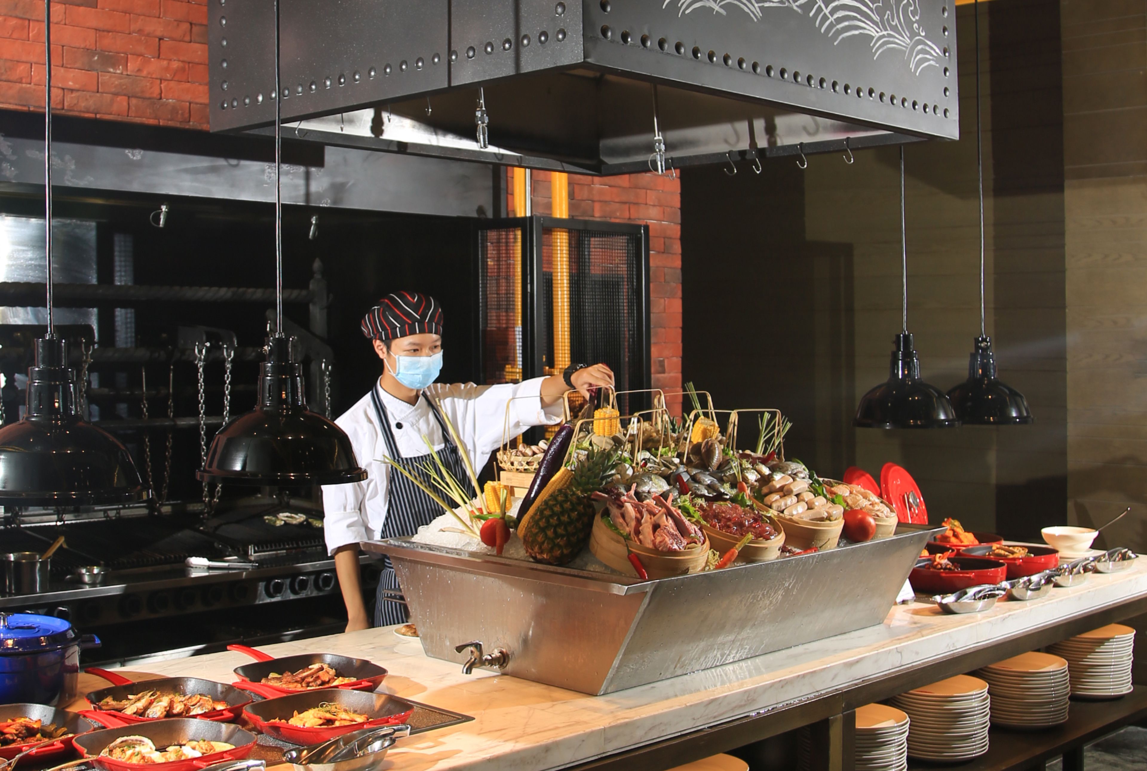 A buffet setup with various dishes, a chef, and kitchen equipment in the background.