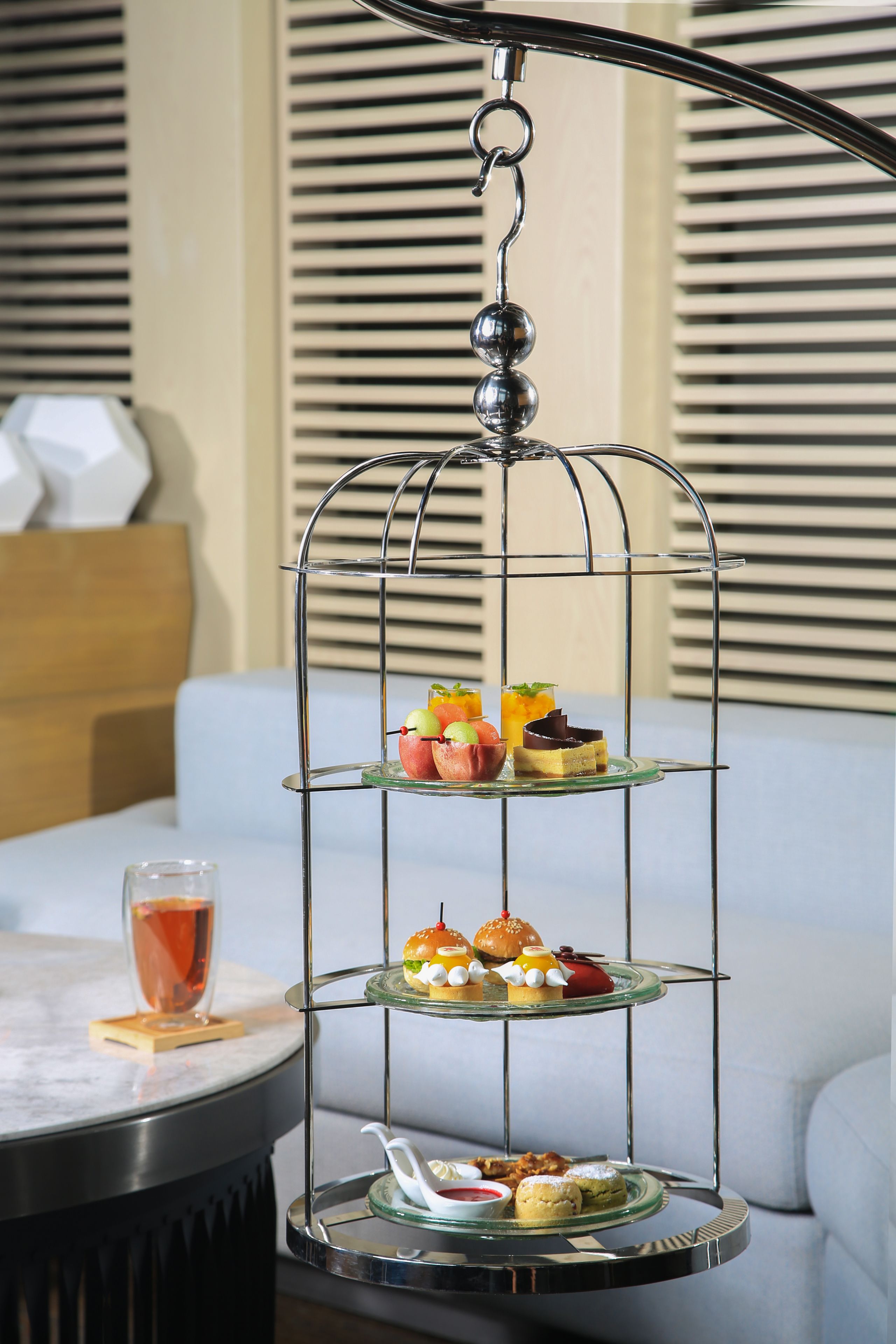 Un présentoir à trois niveaux, garni de diverses pâtisseries, et un verre contenant une boisson, le tout posé sur une table.