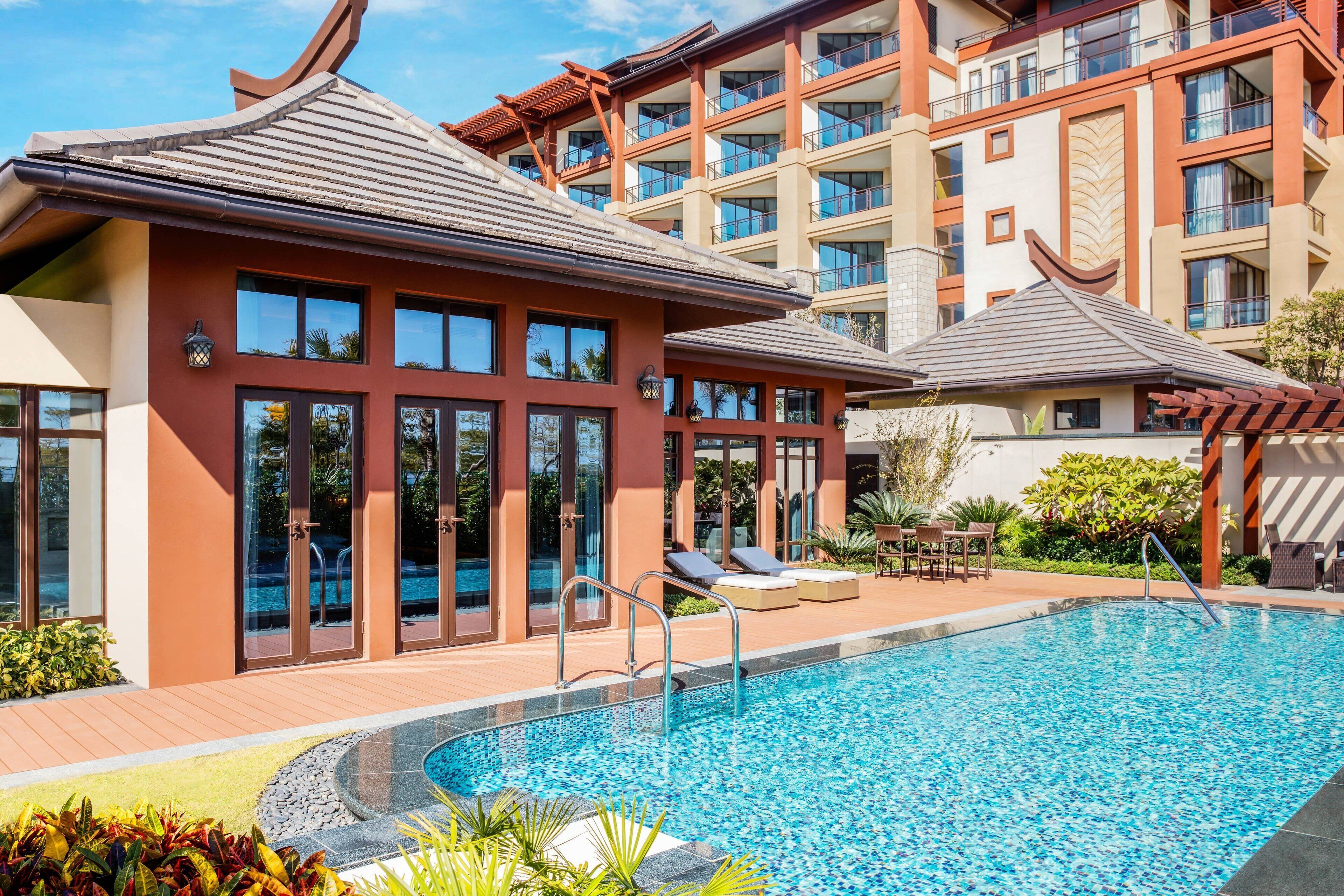 A hotel with a swimming pool, outdoor seating, and a traditional architectural style.
