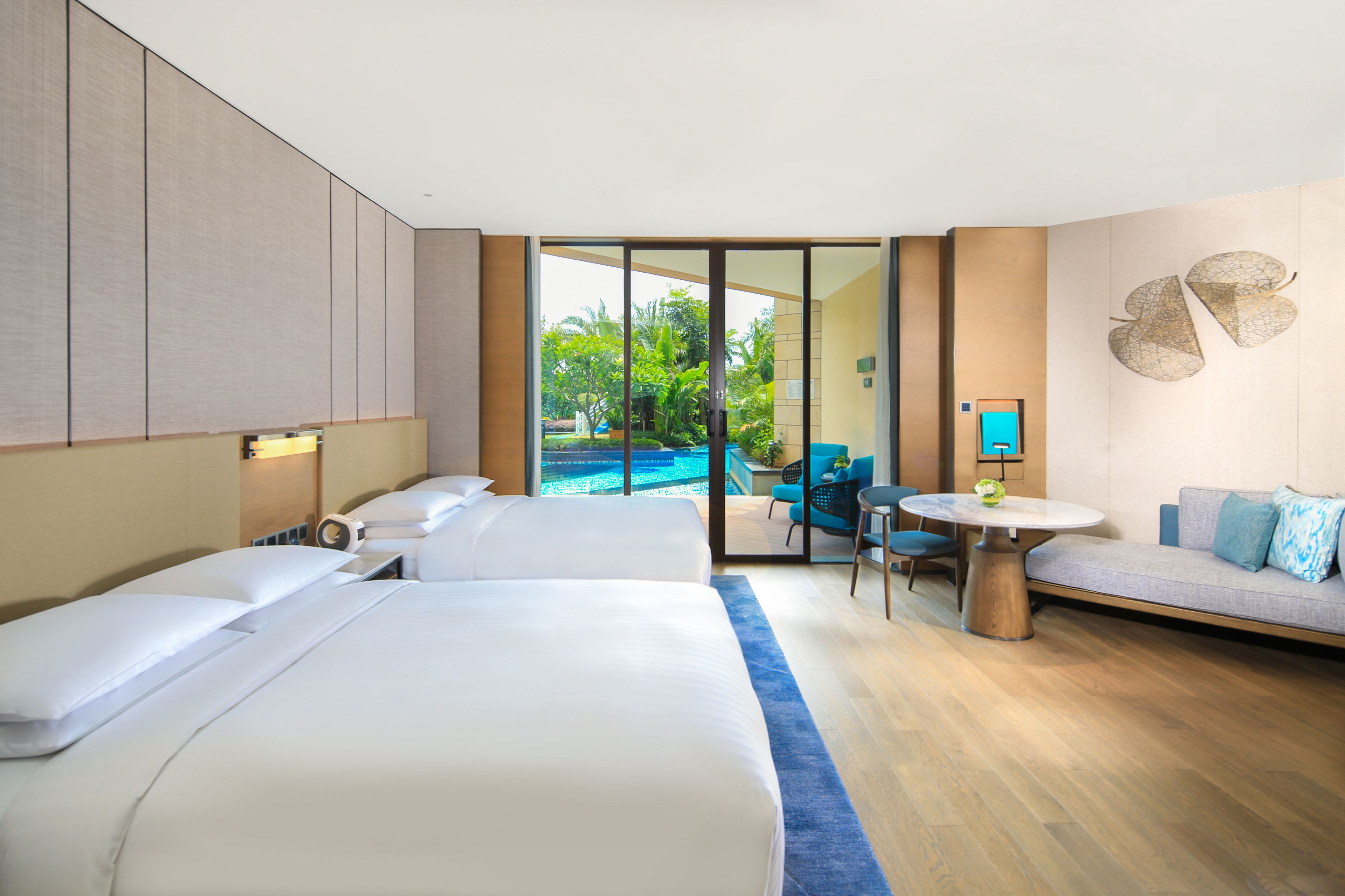 A hotel room with two beds, a sofa, a small table, and a view of a swimming pool.