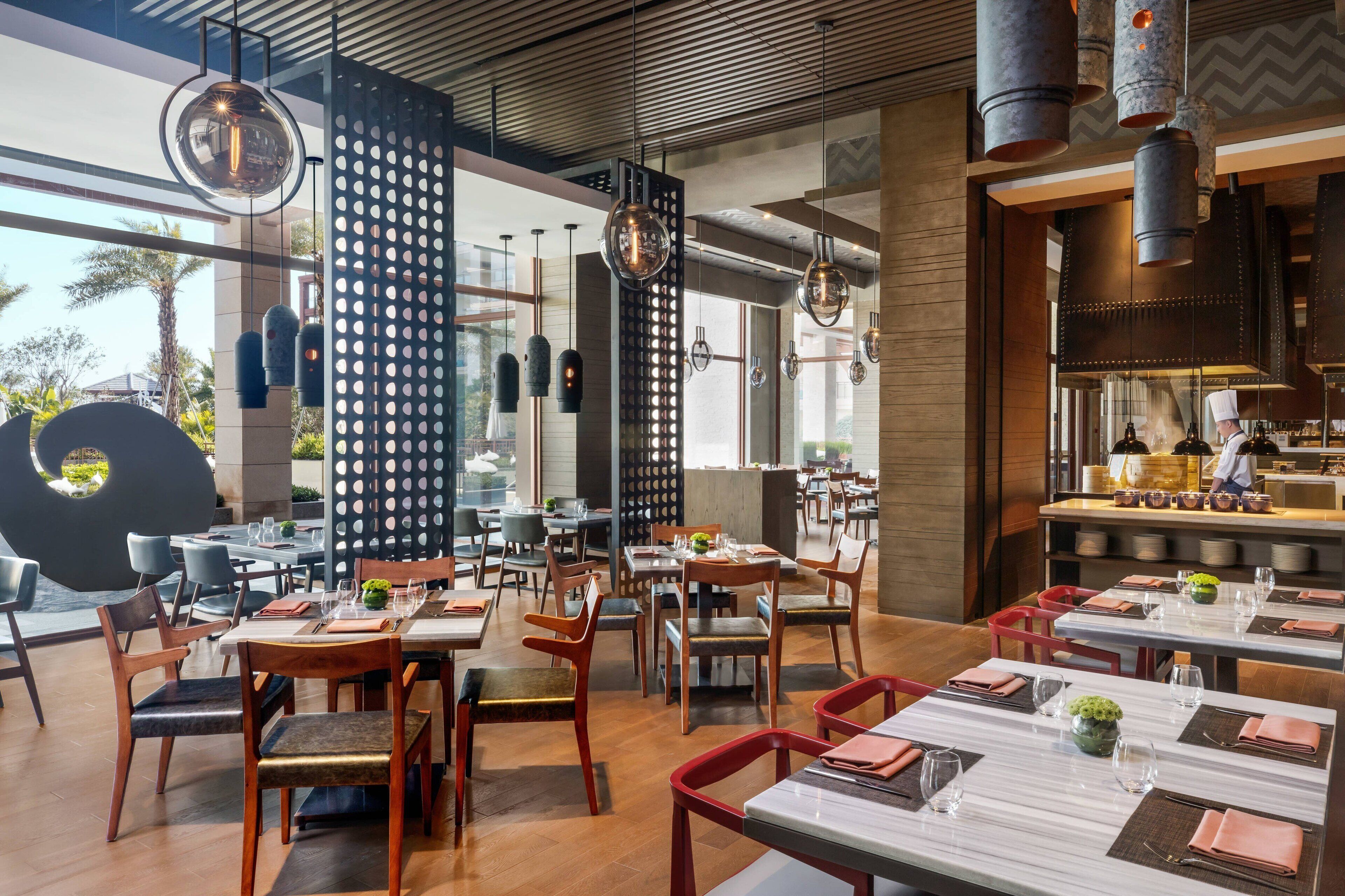 A modern restaurant interior with wooden tables, chairs, and hanging pendant lights.