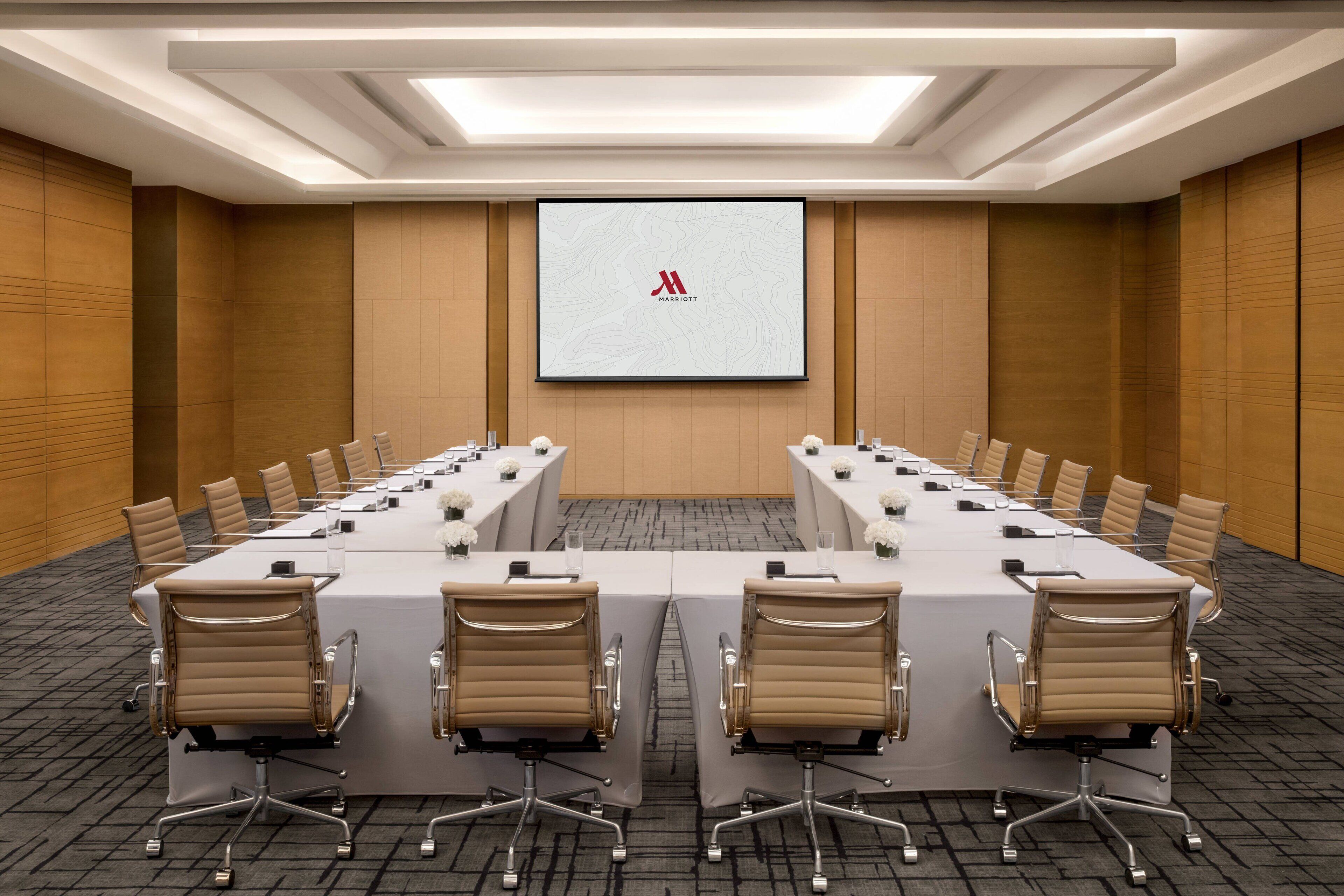 A conference room with a long table, chairs, a projector screen, and a carpeted floor.