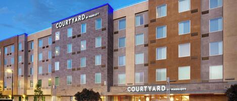 A Courtyard by Marriott hotel with a modern facade, multiple floors, and a parking lot with several cars.