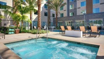 Zona de piscina de hotel con jacuzzi, sillas de descanso y palmeras.