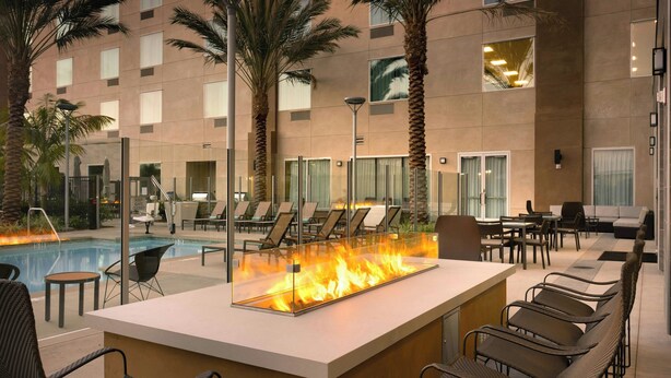 A pool area with a fire feature, lounge chairs, and tables. - Courtyard by Marriott Los Angeles LAX/Hawthorne (Hawthorne)
