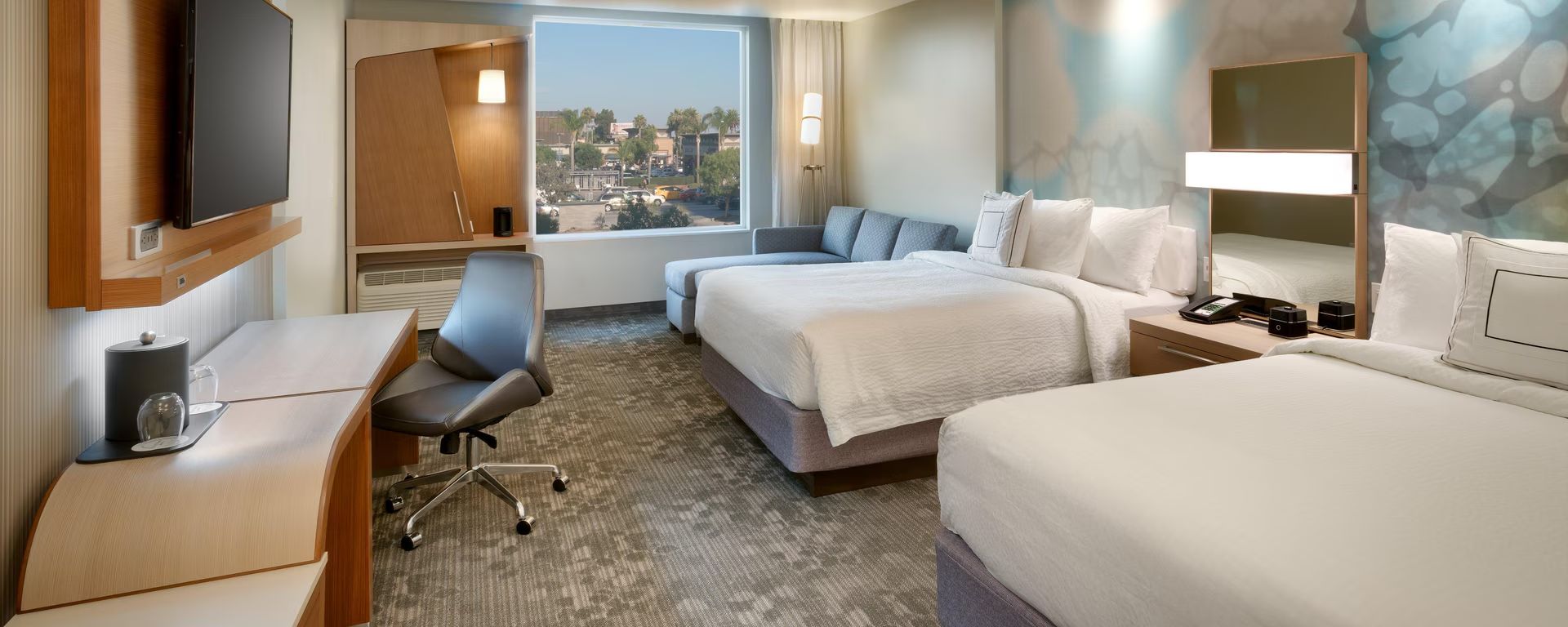 Habitación de hotel con cama, escritorio, silla, televisión y ventana con vista a la ciudad.