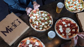 Una mesa con tres pizzas, dos bebidas y una caja con la etiqueta 'Midici'.